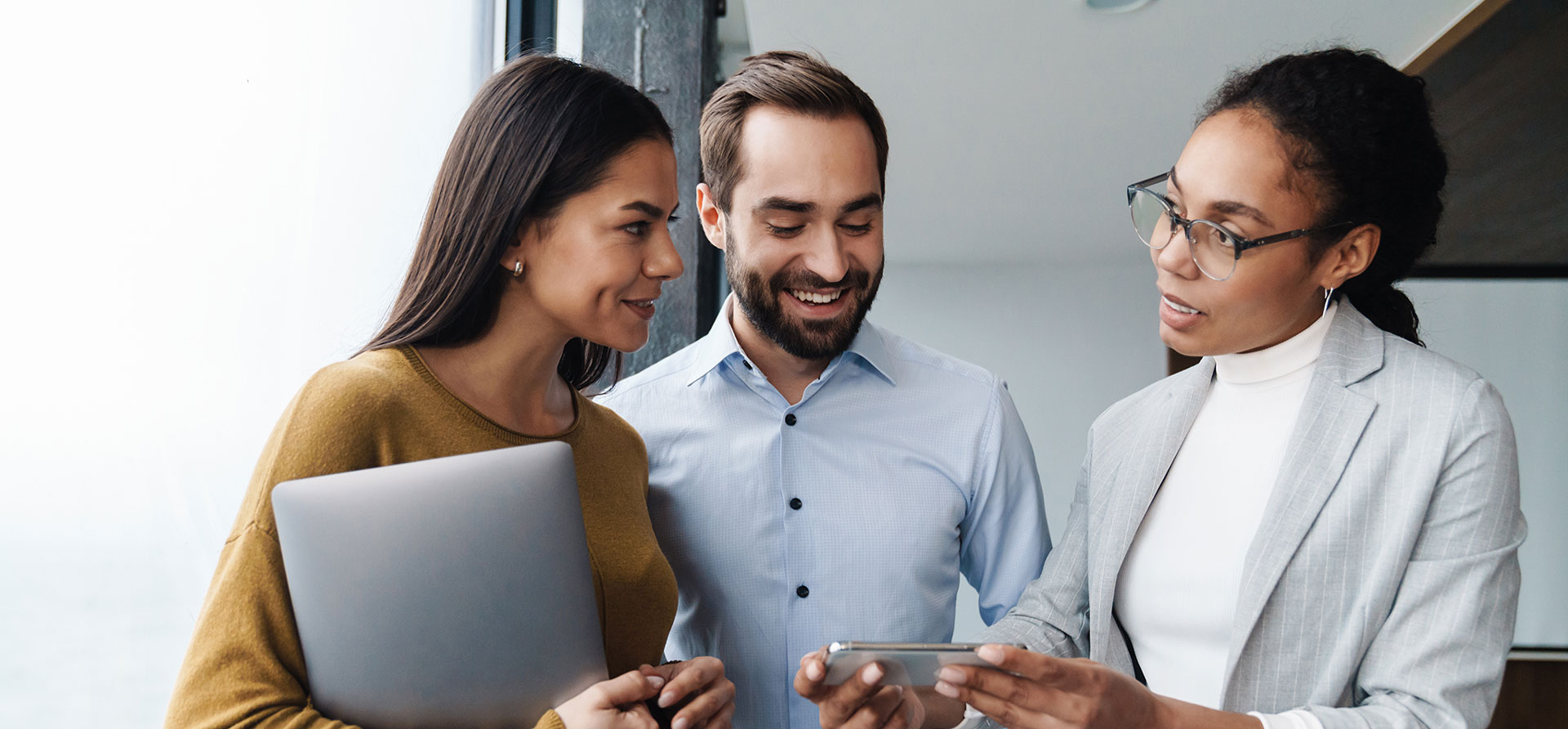 A group of three coworkers smiling at a phone, engaged in a positive and collaborative experience.