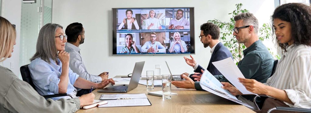 Diverse company employees having online business conference video call on tv screen monitor in board meeting room. Videoconference presentation, global virtual group corporate training concept