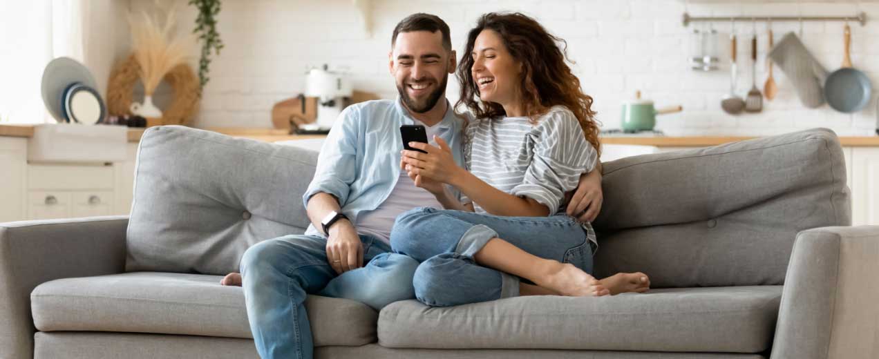 Happy couple sitting on a couch using a mobile phone